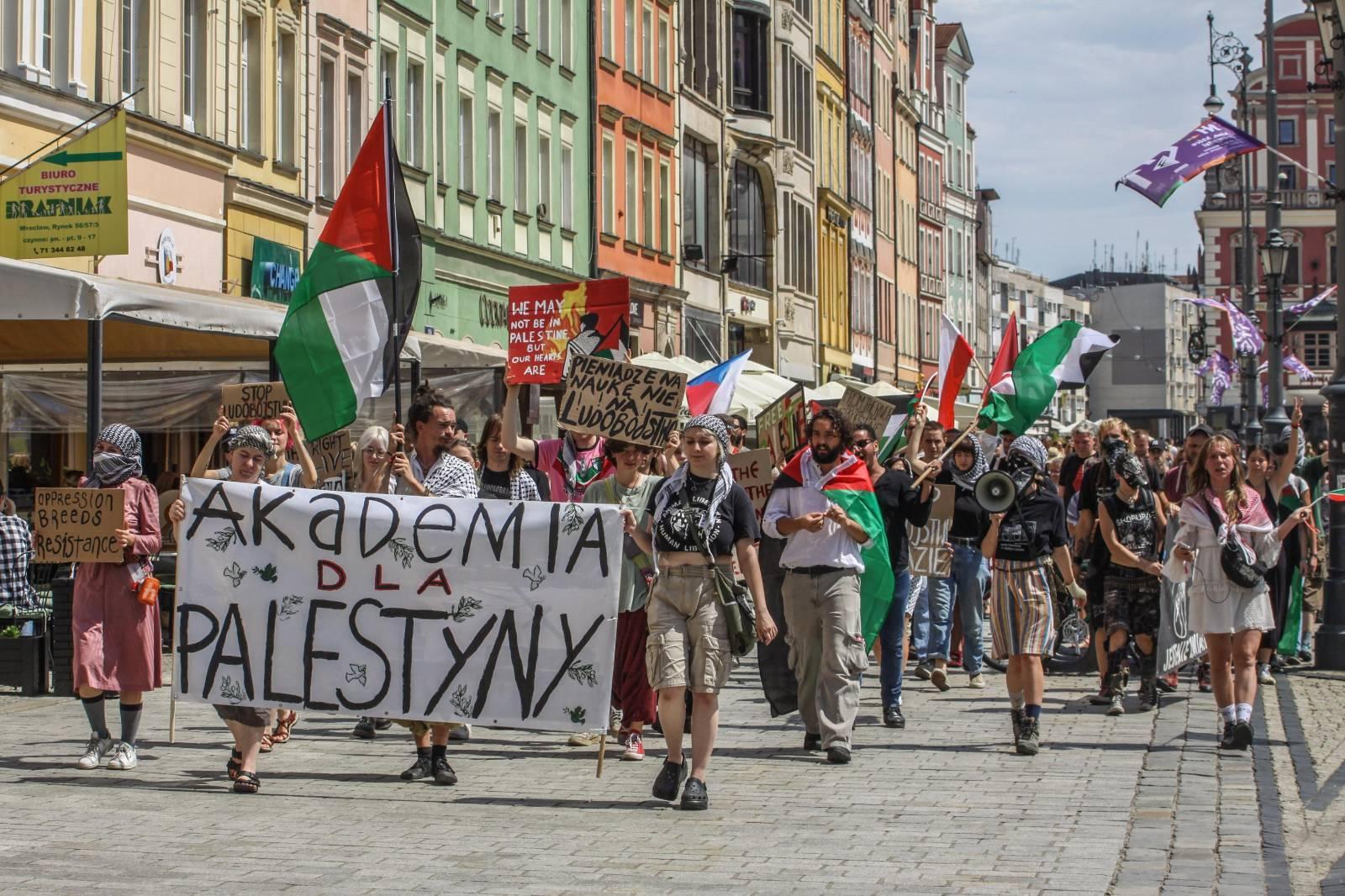 Osoby demonstrujące idą tłumem przez Rynek, z banerem „Akademia dla Palestyny” na przodzie.