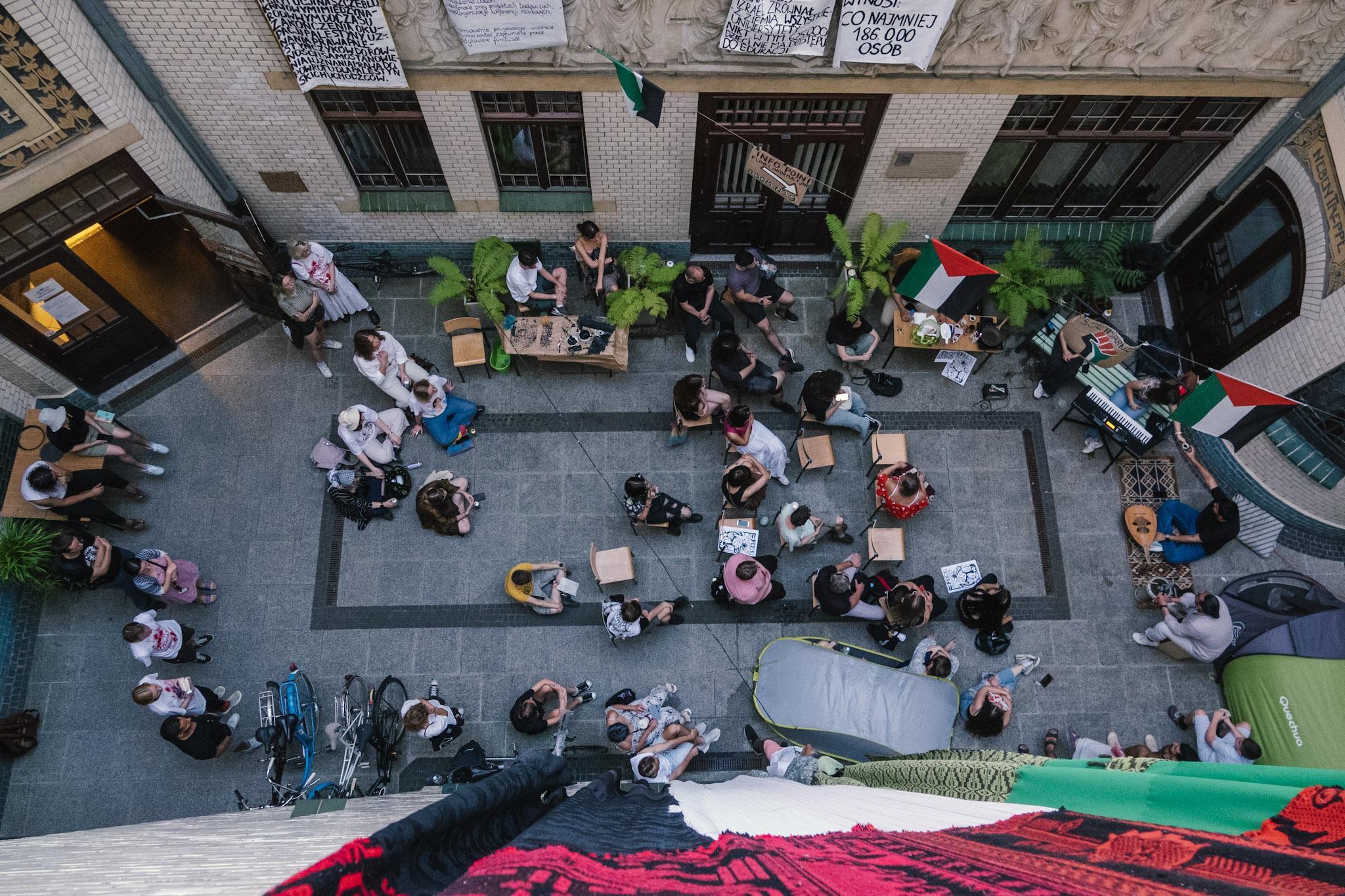 Koncert muzyki arabskiej. Widok z lotu ptaka na patio, gdzie na ziemi i krzesłach siedzą muzycy i słuchacze.