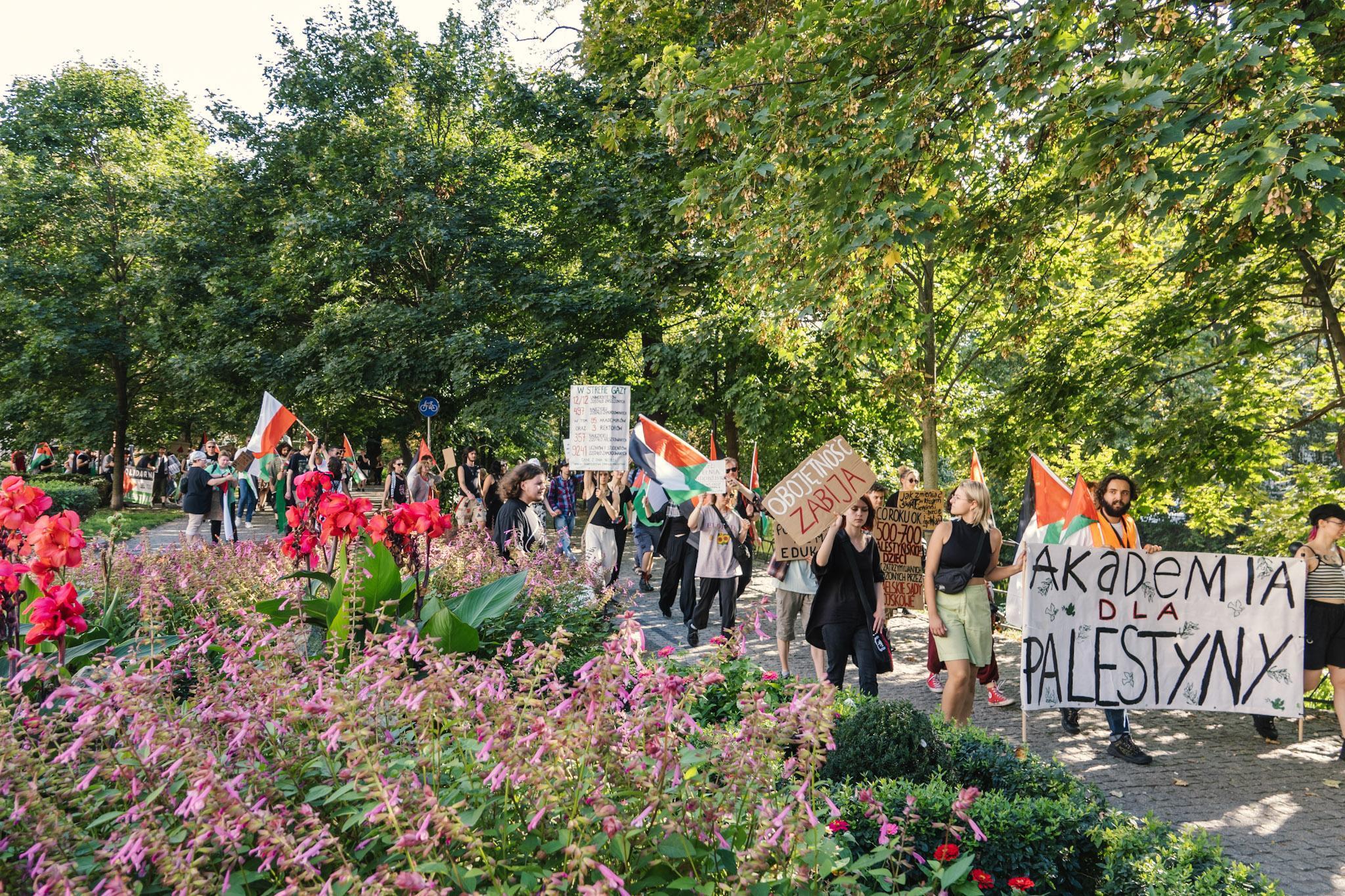 Osoby demonstrujące idące marszem przez park koło fosy Wrocławia.