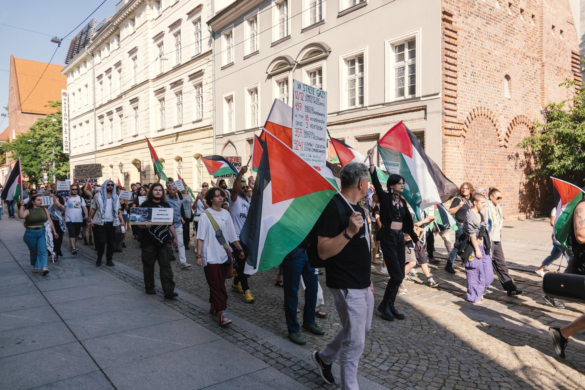 Osoby demonstrujące idące przez ulicę Szewską, pod terenem okupacji.